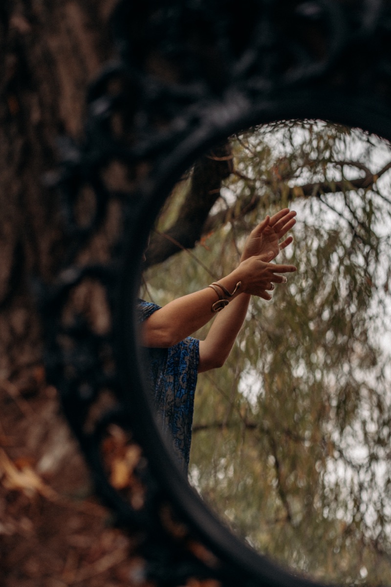 Inge's reflection in a round mirror hanging under a willow tree, hands raised